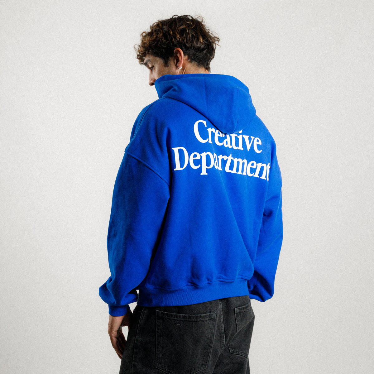 Back of the blue Creative Department hoodie with oversized white wordmark